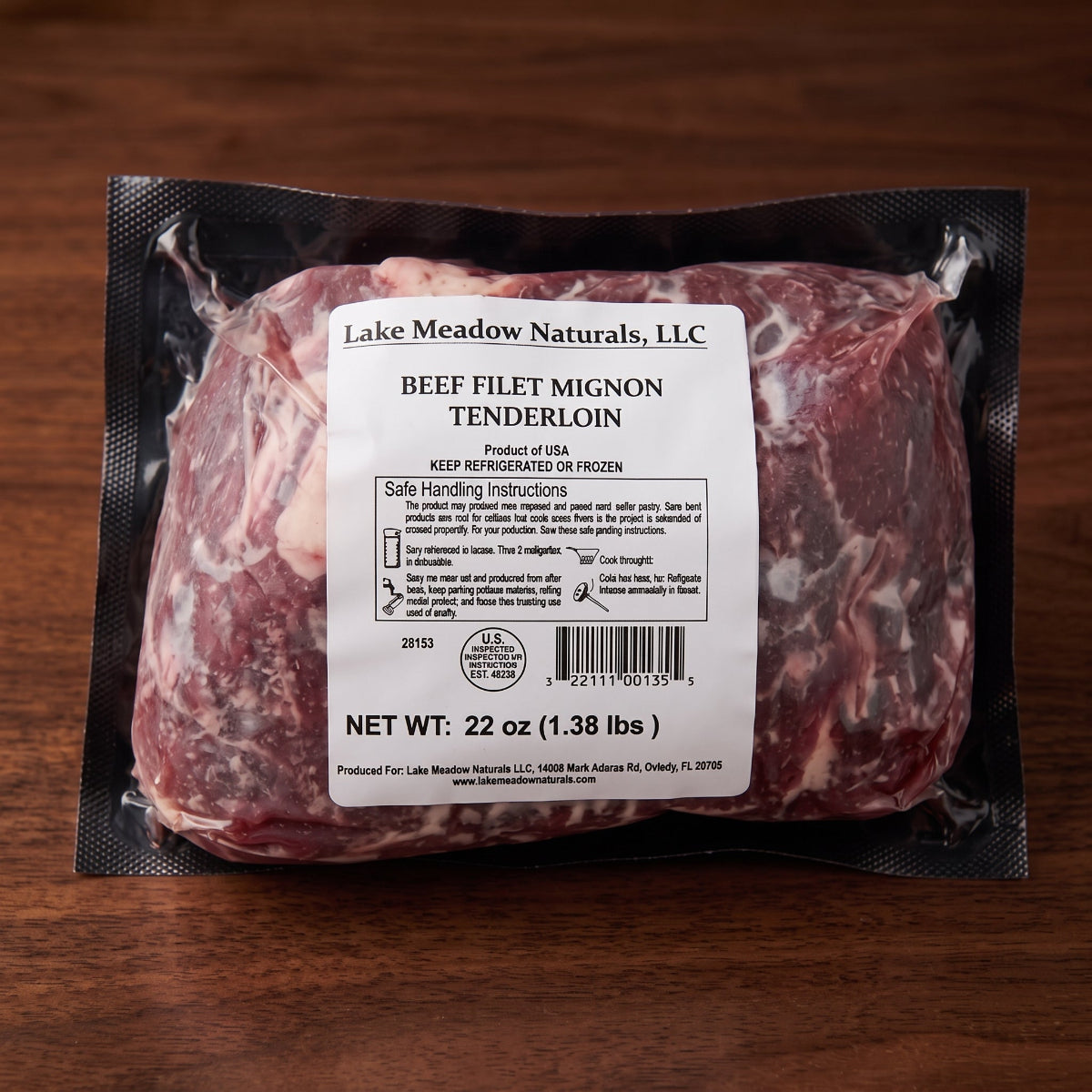 A vacuum-sealed package of Lake Meadow Naturals Beef Filet Mignon Tenderloin on a dark wooden surface. The package is black plastic with a large white label showing product details, weight, and handling instructions.